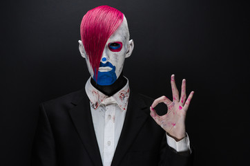 Clown and Halloween theme: Scary clown with pink hair in a black jacket on a dark background in the studio