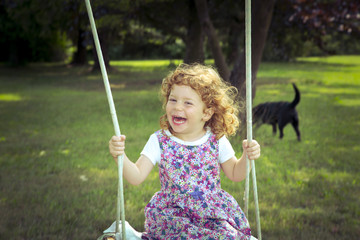 Bambina bionda sorridente sull'altalena con cagnolino sullo sfondo © AP Adobe Contributor
