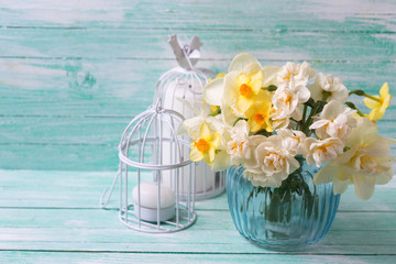Bright  narcissus flowers in blue vase and candles  on turquoise painted wooden planks. Selective focus. Place for text..