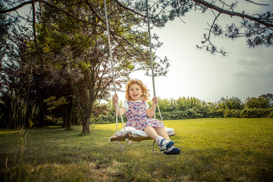 Bambina bionda sorridente sull'altalena con sfondo parco giardino