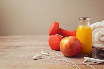 Fitness concept with dumbbells, bottle of juice and smartphone on wooden background