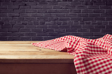 Wooden table background with red checked tablecloth over black brick wall