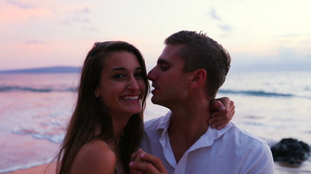 Young Cute Brunette Couple Kissing and Posing for Camera on the Beach at Sunset