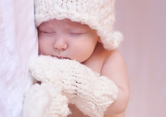 Fototapeta na wymiar Sleeping baby wearing knitted mittens and hat in room. Bed time. Childhood. 