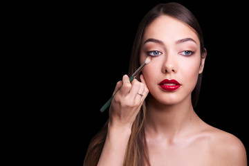 close portrait of beautiful girl making make up. Isolated on black background. Copy space.