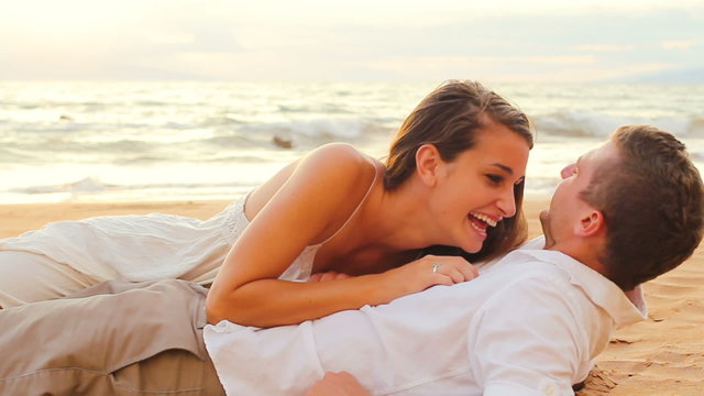 A woman lies on top of man as they play and kiss on the beach
