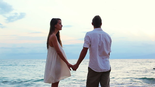 Honeymoon Couple Loving on the Beach at Sunset. Holding Hands and Walking Towards Water.
