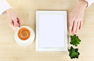 Hands with tablet and cup of coffee, on wooden table