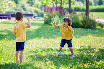 Obraz premium Two children in the park blowing and chasing soap bubbles and ha