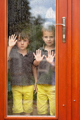 Two little boy, wearing same clothes looking through a big glass