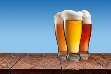Different beer in glasses on wooden table and blue background