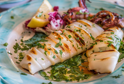 Grilled Squid With Lemov And Vegetables On Color Plate At Italian Restaurant On Amalfi Coast.