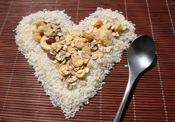 Rice and muesli laid out in a heart shape on bamboo napkin with a spoon 