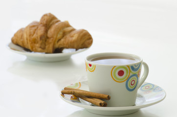 Tea in white mug with cinnamon and croissant