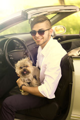Young man with cute dog in cabriolet, outdoors