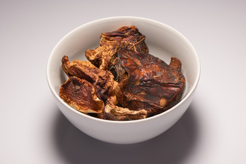 Dried mushrooms in white ceramic bowl on white background