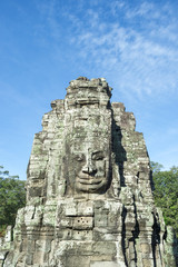 Naklejka premium Angkor Wat Temple of Bayon stone face sculptures in front of green trees under blue sky 