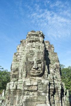 Angkor Wat Temple of Bayon stone face sculptures in front of green trees under blue sky 