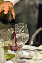 Man's hand pouring red wine from bottle into a glass