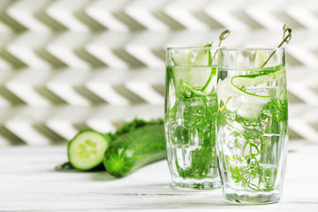 Glasses with fresh organic cucumber water on wooden table, on light background