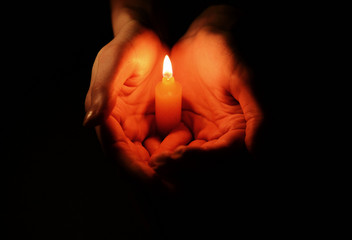 Candle in female hands on black background