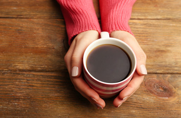 Fototapeta na wymiar Female hands holding cup of coffee on wooden background