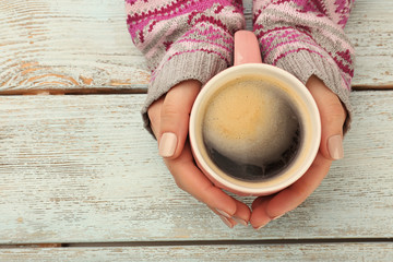 Female hands holding cup of coffee on wooden background