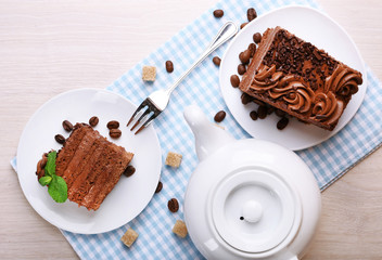 Tasty pieces of chocolate cake with lump sugar and coffee beans near teapot on wooden table background