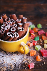 Cinnamon sticks in cup with sugar and dried fruits on wooden table background