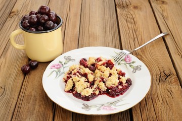 Piece of delicious homemade cherry crumble with fork in white pl
