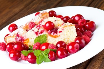 Fruit pie and cherries with raspberries on white plate