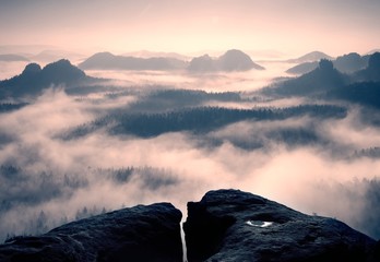 Dreamy daybreak on the top of the rocky mountain with the view into misty valley