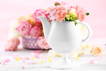 Composition with beautiful spring flowers in teapot on light pink background
