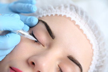 Cosmetologist applying permanent make up on eyes, close-up