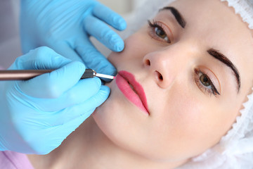 Cosmetologist applying permanent make up on lips