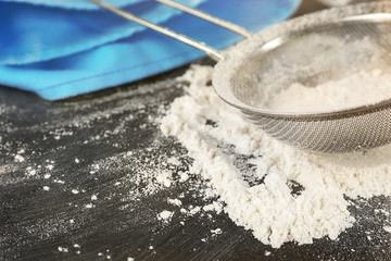 Sifting flour through sieve on wooden table, closeup