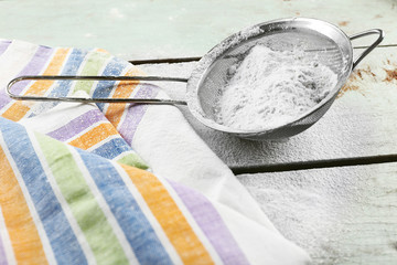 Sifting flour through sieve on wooden table, closeup