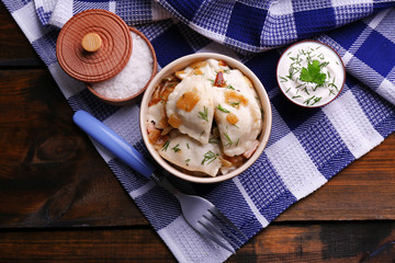Tasty dumplings with fried onion in brown bowl, on wooden background