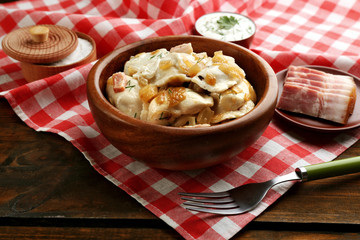 Tasty dumplings with fried onion in brown bowl, on wooden background