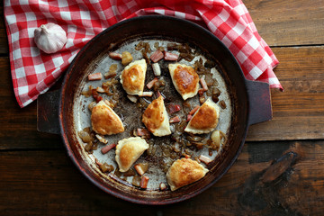 Fried dumplings with onion and bacon in frying pan, on wooden table background