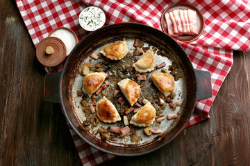 Fried dumplings with onion and bacon in frying pan, on wooden table background