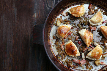 Fried dumplings with onion and bacon in frying pan, on wooden table background