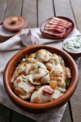 Fried dumplings with onion and bacon in frying pan, on wooden table background
