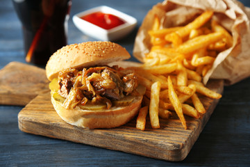 Tasty burger and french fries on plate, on wooden table background. Unhealthy food concept