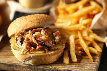 Tasty burger and french fries on plate, on wooden table background. Unhealthy food concept