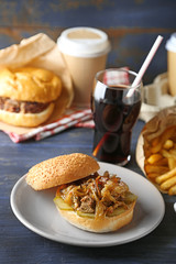 Tasty burger and french fries on plate, on wooden table background. Unhealthy food concept