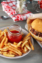 Tasty burger and french fries on plate, on wooden background. Unhealthy food concept