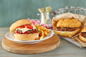 Tasty burger and french fries on plate, on wooden background. Unhealthy food concept