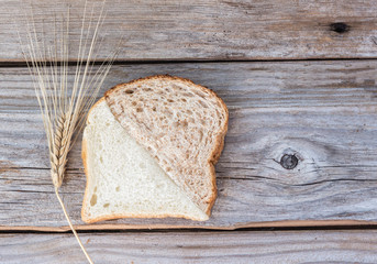 horizontal image of a white slice and a whole wheat slice of bread cut at an angle and put together as one slice placed on a rustic wood background with lots of room for text.