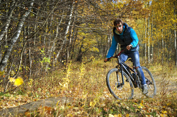 Fototapeta na wymiar Cyclist extreme riding mountain bike through impassable dried bushes in wild autumn colorful forest 